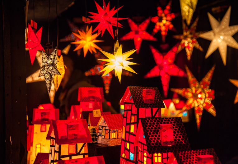 Beleuchtete Dekosterne und -häuser an einem Stand auf dem Weihnachtsmarkt